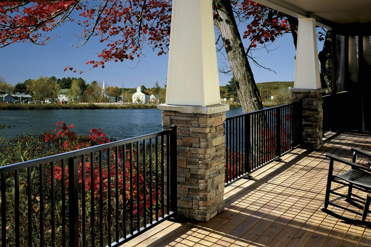 Black Westbury Tuscany railing on a lakeside porch with stone columns and autumn foliage